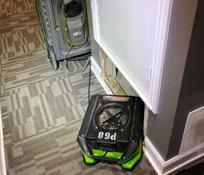 green air mover sitting on blue carpet pointed in an open wall cavity 